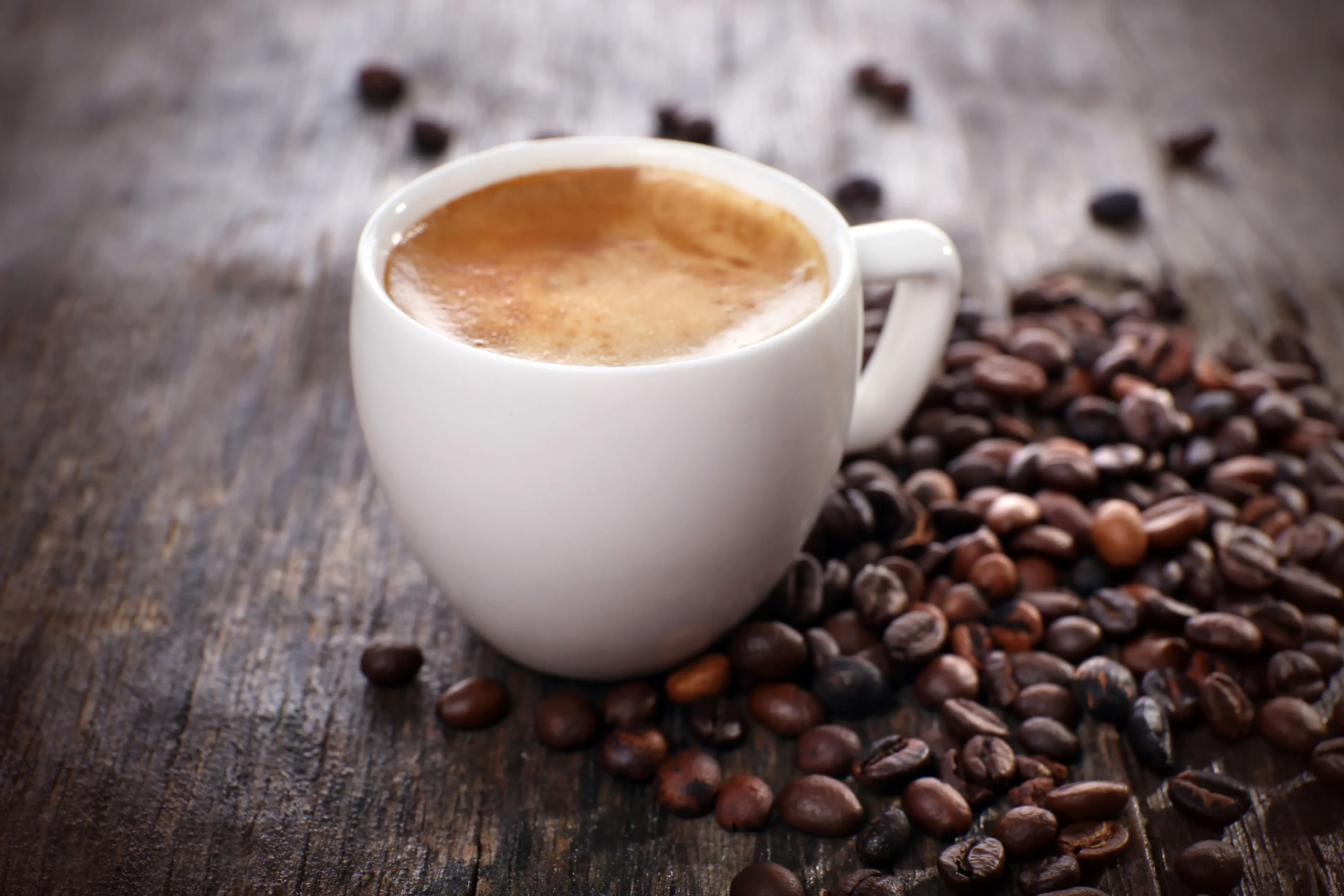 primo piano di un caffè schiumato in mezzo a ranti chicci di caffè