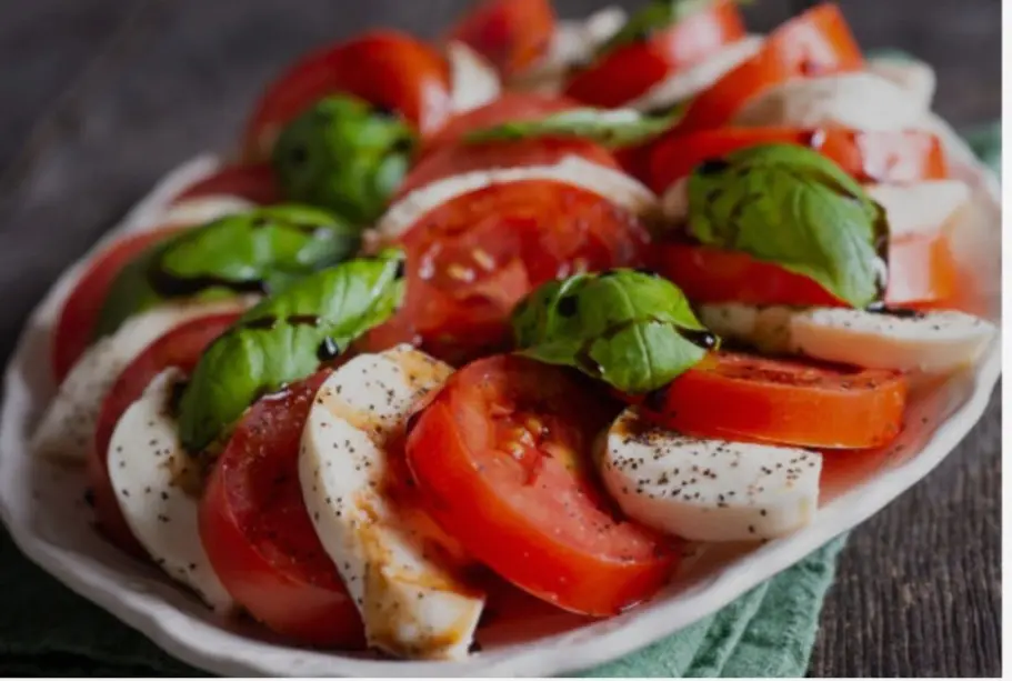 piatto estivo e salutare composto da mozzarelle e pomodori, disposti a modo di ventagli con sopra varie foglie com profumo